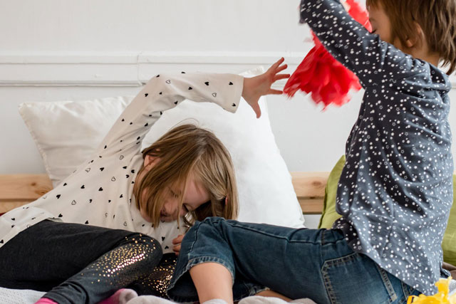 Zwei Kinder streiten auf dem Bett und hauen sich.