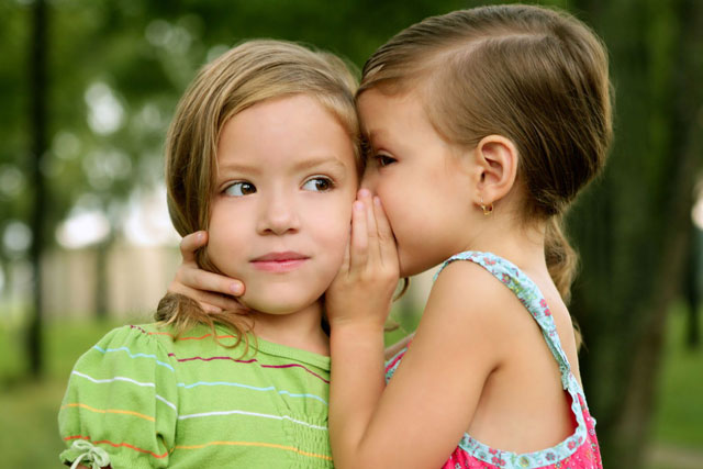 Zwei Kinder flüstern sich etwas ins Ohr